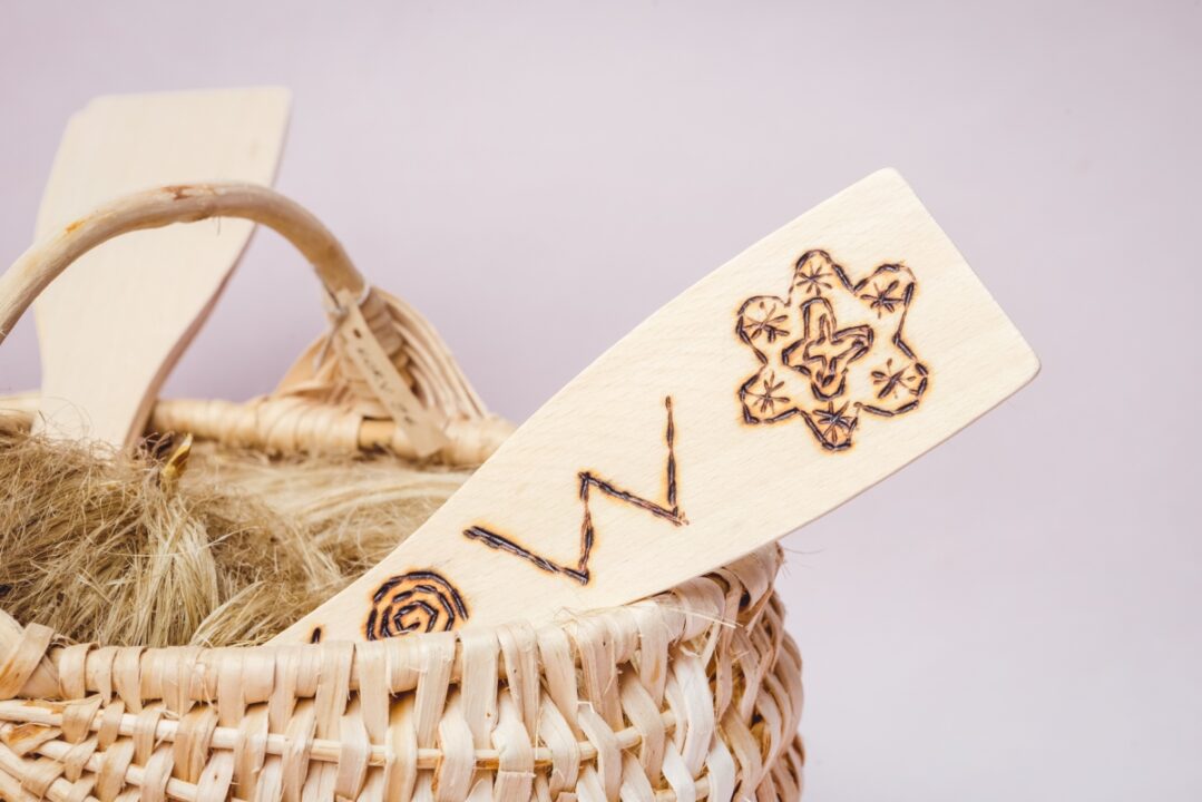 Punutud korvi seest paistab välja lapik puust ese. Eseme peale on põletatud muster.