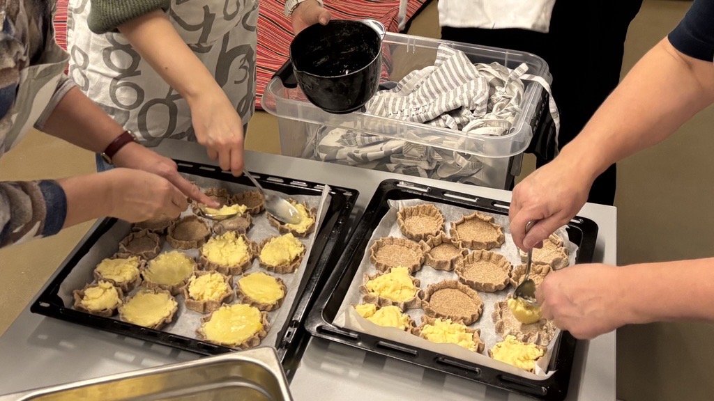 Kaks ajuplaati täis lahtisi pirukaid. Kolm inimest pirukaid valmistamas.